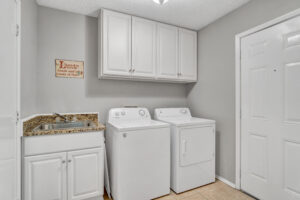 A white laundry room with two machines and cabinets.