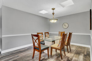 A dining room table with six chairs and a clock on the wall.