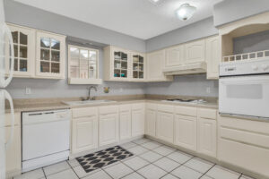 A kitchen with white cabinets and tile floors.